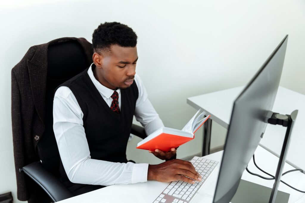 Business professional reading a book while working at the computer in the office.